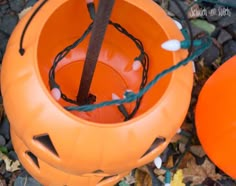 an orange plastic pumpkin sitting on top of some leaves and string wrapped around the inside of it