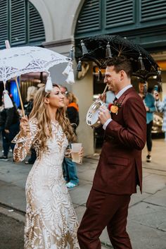 a man and woman are walking down the street with umbrellas over their heads while holding drinks