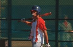 a young man holding a baseball bat while wearing a helmet and batting gloves on the field