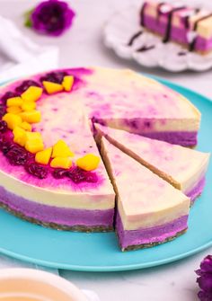 a blue plate topped with a cake covered in purple and yellow frosting next to flowers