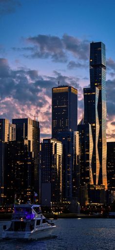 a boat is in the water near some tall buildings at dusk with purple and blue clouds