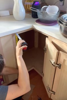 a woman is holding a knife in her kitchen cupboards and looking into the sink