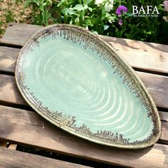 a green plate sitting on top of a wooden table next to flowers and bushes in the background