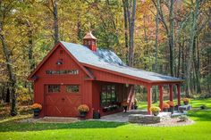 a red barn in the woods with lots of trees and flowers on it's side