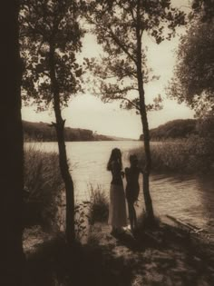 two people are standing by the water near some trees