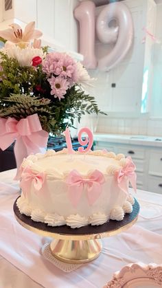 a white cake with pink bows on top sitting on a table next to a vase filled with flowers