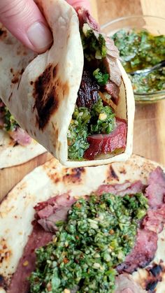 a person is holding up a burrito with meat and vegetables in it on a wooden table