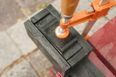 an orange handle is on top of a black piece of wood that has been placed on a red bench