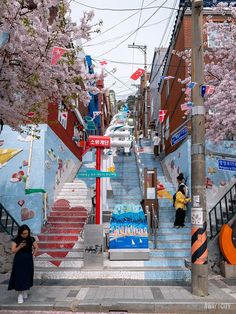 people are walking up and down the stairs in front of some buildings with cherry blossoms on them