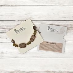 a bracelet with brown beads on top of a white wooden table next to a business card