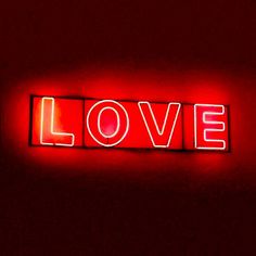 a red neon sign that says love in the middle of it's letters on a wall