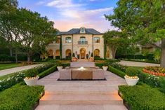 a large house with a fountain in the middle of it's front yard, surrounded by greenery and trees