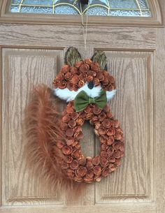 a wreath is hanging on the front door with a fox head made out of pine cones