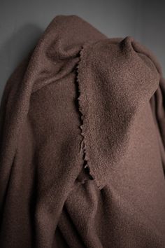 a brown coat is hanging on the wall with it's hood pulled back and there are holes in the fabric