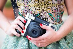 a woman holding a camera in her hands with red nail polishes and a patterned dress