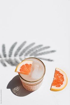 grapefruit cocktail with orange slices on the rim and in a glass next to a palm leaf