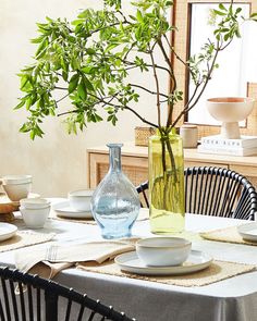 a dining room table with plates, bowls and vases on it in front of a window