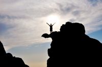 a person standing on top of a mountain with their arms up in the air above them