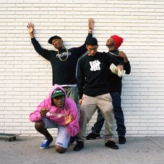 three young men standing next to each other in front of a white brick wall with their hands up