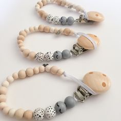 two wooden pacifiers are attached to necklaces on a white surface with grey and white beads