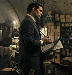 a man in a suit and tie writing on a piece of paper while standing in a warehouse