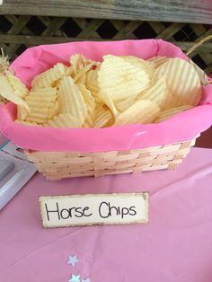 a pink basket filled with chips sitting on top of a table next to a sign that says horse chips