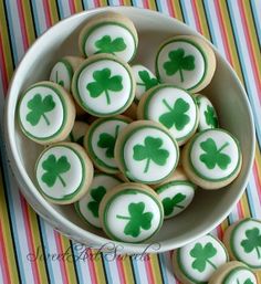 a bowl filled with green shamrock cookies sitting on top of a striped table cloth next to a cup