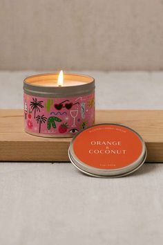 an orange coconut candle sitting on top of a wooden tray next to a small tin