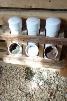 four jars with spices in them sitting on a wooden shelf next to wood shavings