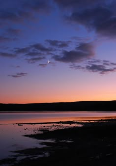 the sky is purple and blue as the sun sets on the horizon with clouds in the background