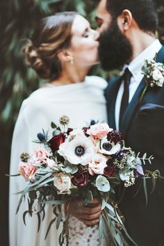 a bride and groom kissing in front of some trees with their bouquets on them