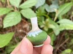 a hand holding a small green and white vase