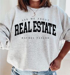 a woman wearing a sweatshirt that says ask me about real estate and has her hands on her hips