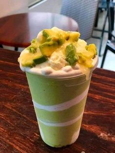 a green and white cup filled with food on top of a wooden table at a restaurant