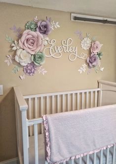 a baby crib in a nursery with flowers on the wall and name sign above it