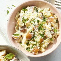 a bowl filled with potato salad next to a fork and spoon on a white table