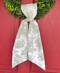 a green and white wreath on a red door with a bow hanging from it's side