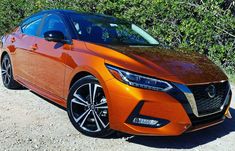 an orange car parked in front of some bushes