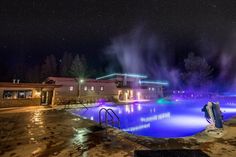 an outdoor swimming pool at night with lights on the buildings and trees in the background