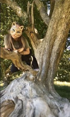 a woman sitting on top of a tree branch with a cat mask over her face