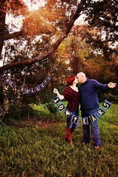 a man and woman standing in the grass with their arms around each other while holding up letters