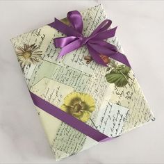 an origami box with purple ribbon tied around it and flowers on the side