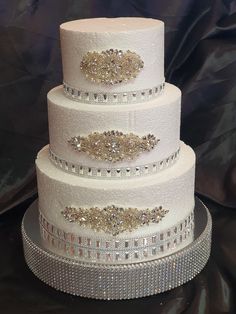 a three tiered white wedding cake with gold and silver decorations on it's sides