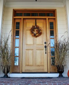 a front door with two plants and a wreath on it