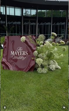 a large sign sitting in the middle of a lush green field next to a building