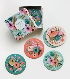 four coasters with colorful floral designs and a box on the table next to them