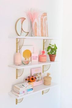 three shelves with books, vases and other items on them against a white wall