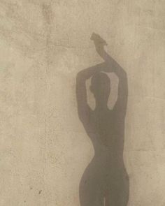 the shadow of a woman holding a bird on her head is cast against a concrete wall