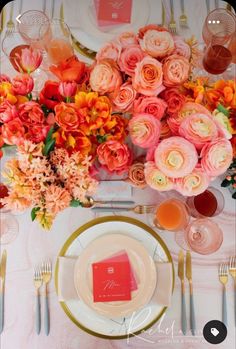 the table is set with pink and orange flowers, gold place settings, and silverware