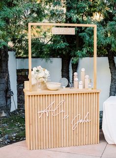 a wooden bar with white flowers and bottles on the counter at an outdoor wedding reception